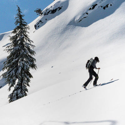 A backcountry skier ascends a steep, snowy mountain slope using an ultralight Hyperlite Mountain Gear backpack.