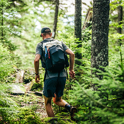 Fastpacker wearing a black Hyperlite Mountain Gear Contour 32 pack while running on a lush, technical forest trail.