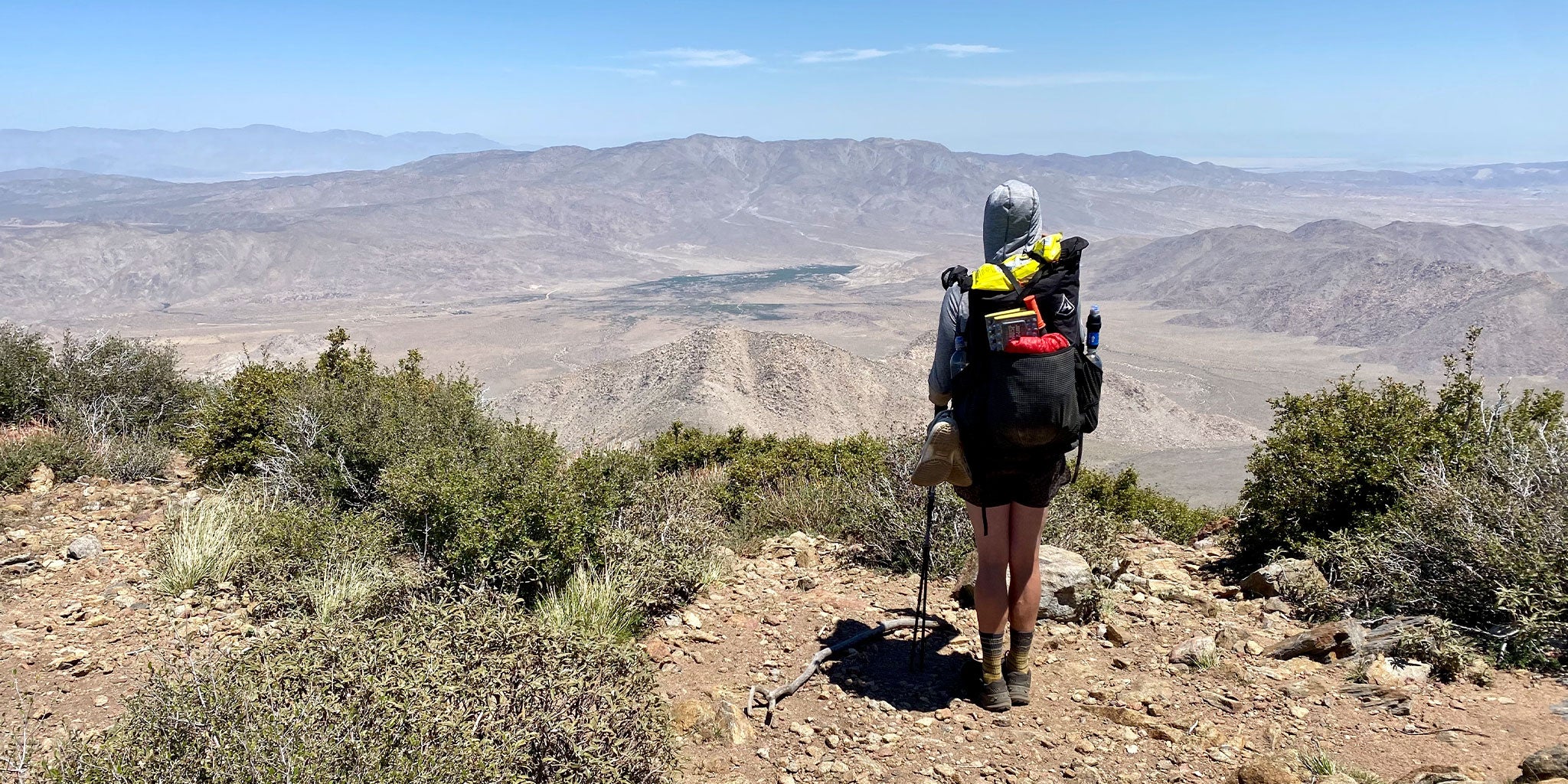 A hiker on a trail looking down at a valley.
