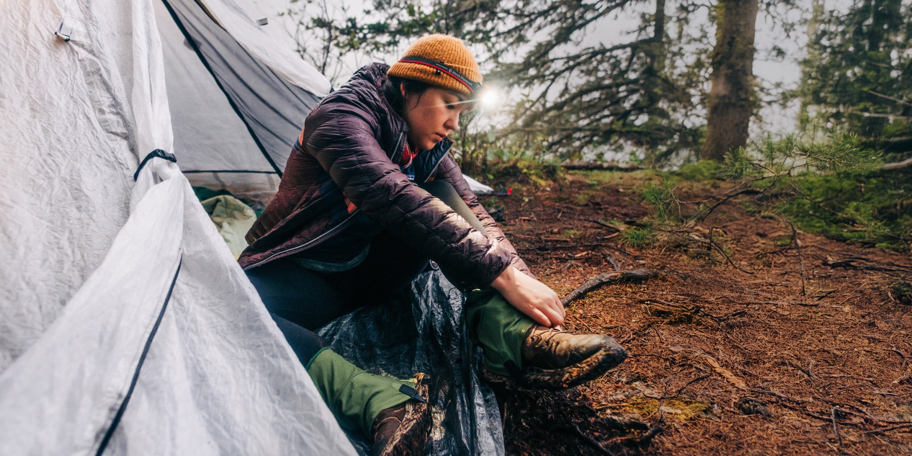 Person sitting by a tent in a forest setting