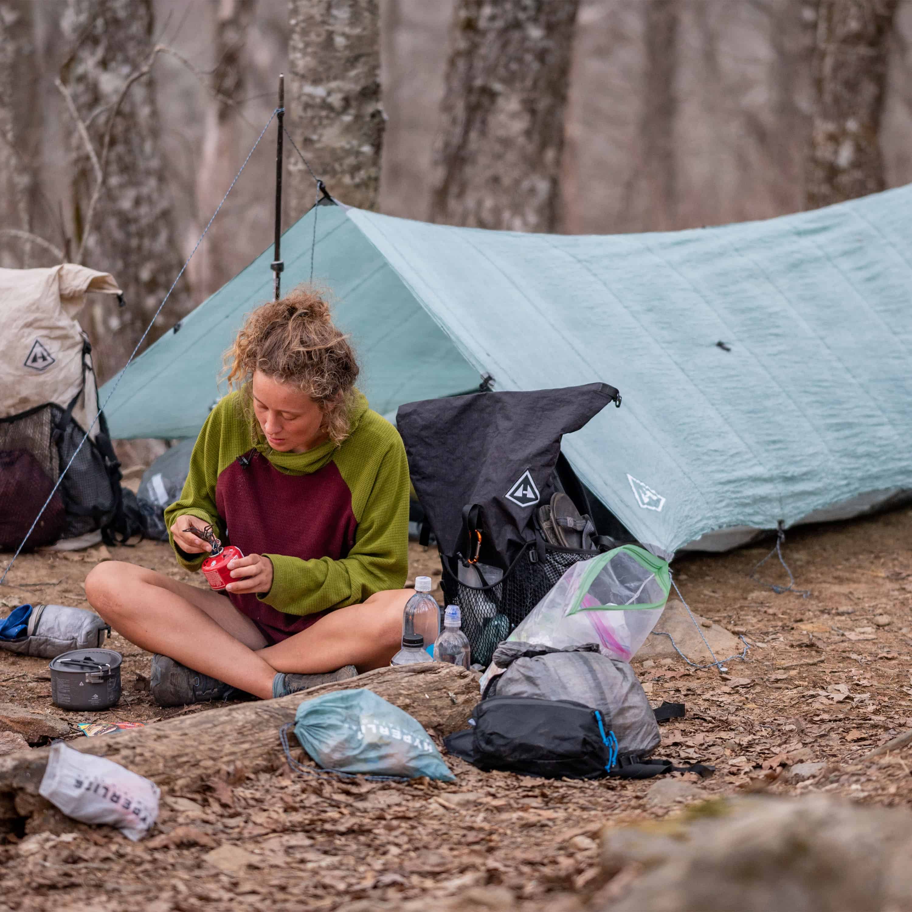 Camper setting up cooking burner in front of their Hyperlite Mountain Gear Flat Tarp in Spurce Green