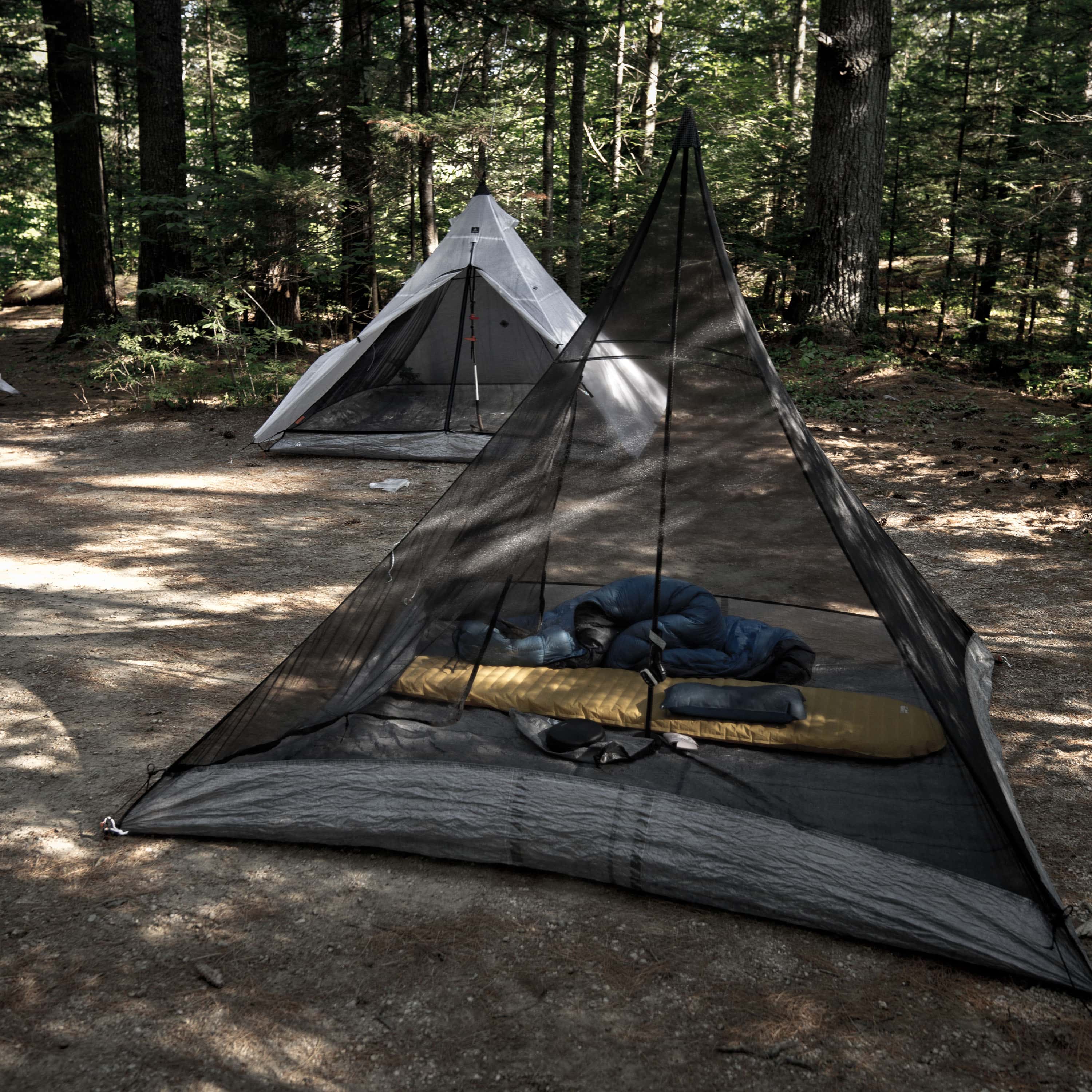 Exterior view of Hyperlite Mountain Gear Shelters UltaMid 2 Insert with DCF11 Floor without tent in a wooded setting. A white UltaMid 2 with insert sits in the background.