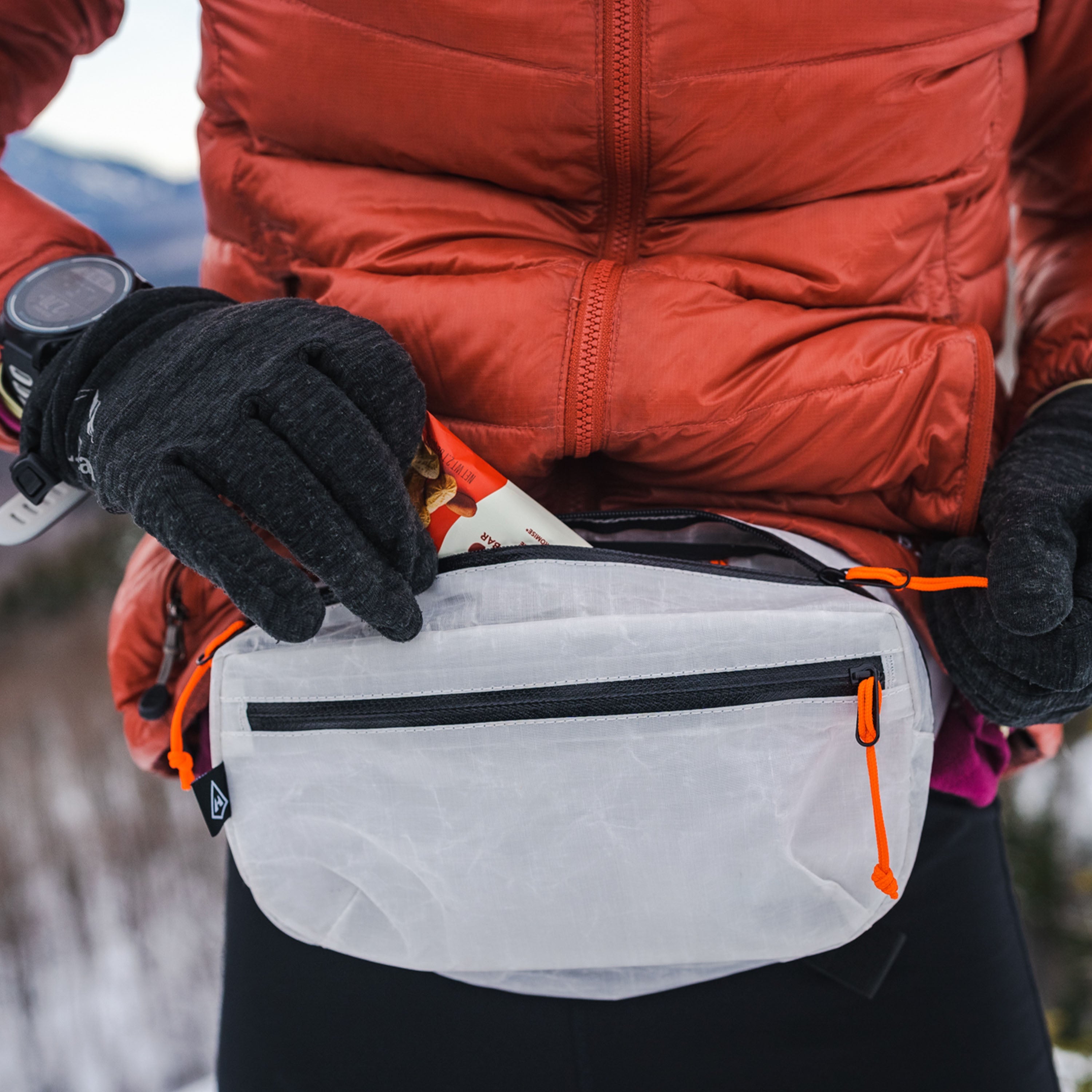 Front view shot of a hiker putting a protein bar in Hyperlite Mountain Gear's White Versa