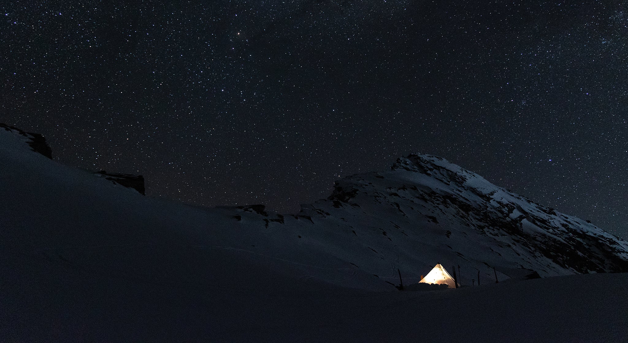 A tent under the stars on a snow covered mountain.