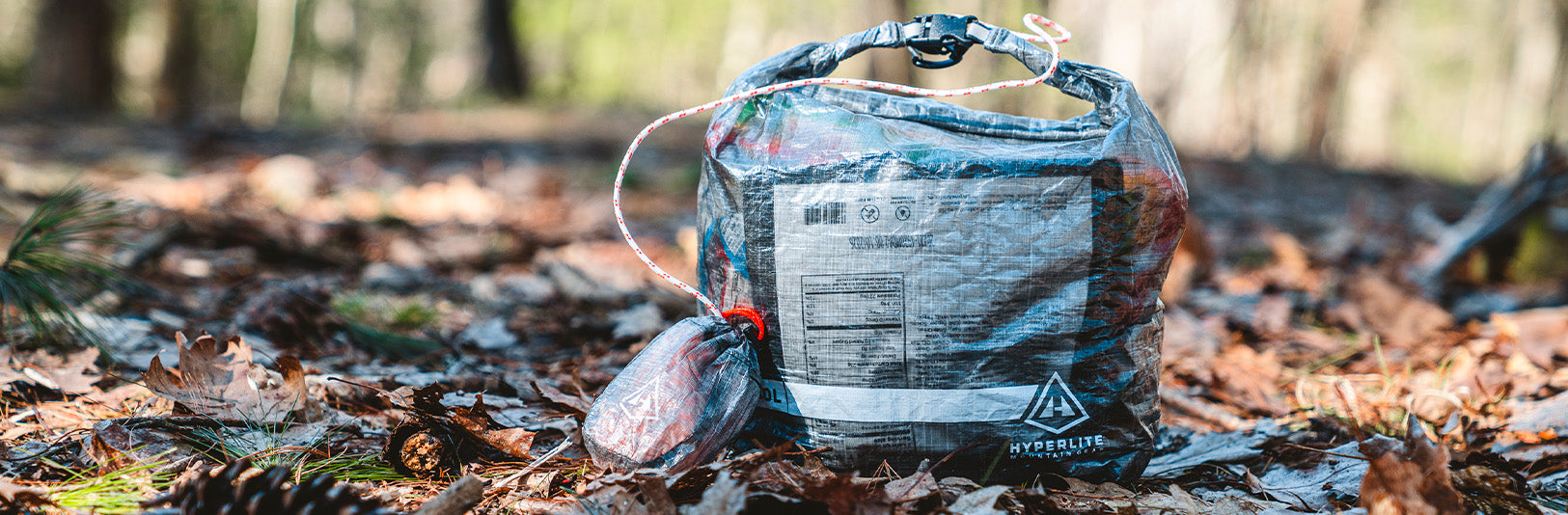 A lightweight, multicolored backpack made from durable material, sitting on a forest floor covered in autumn leaves.