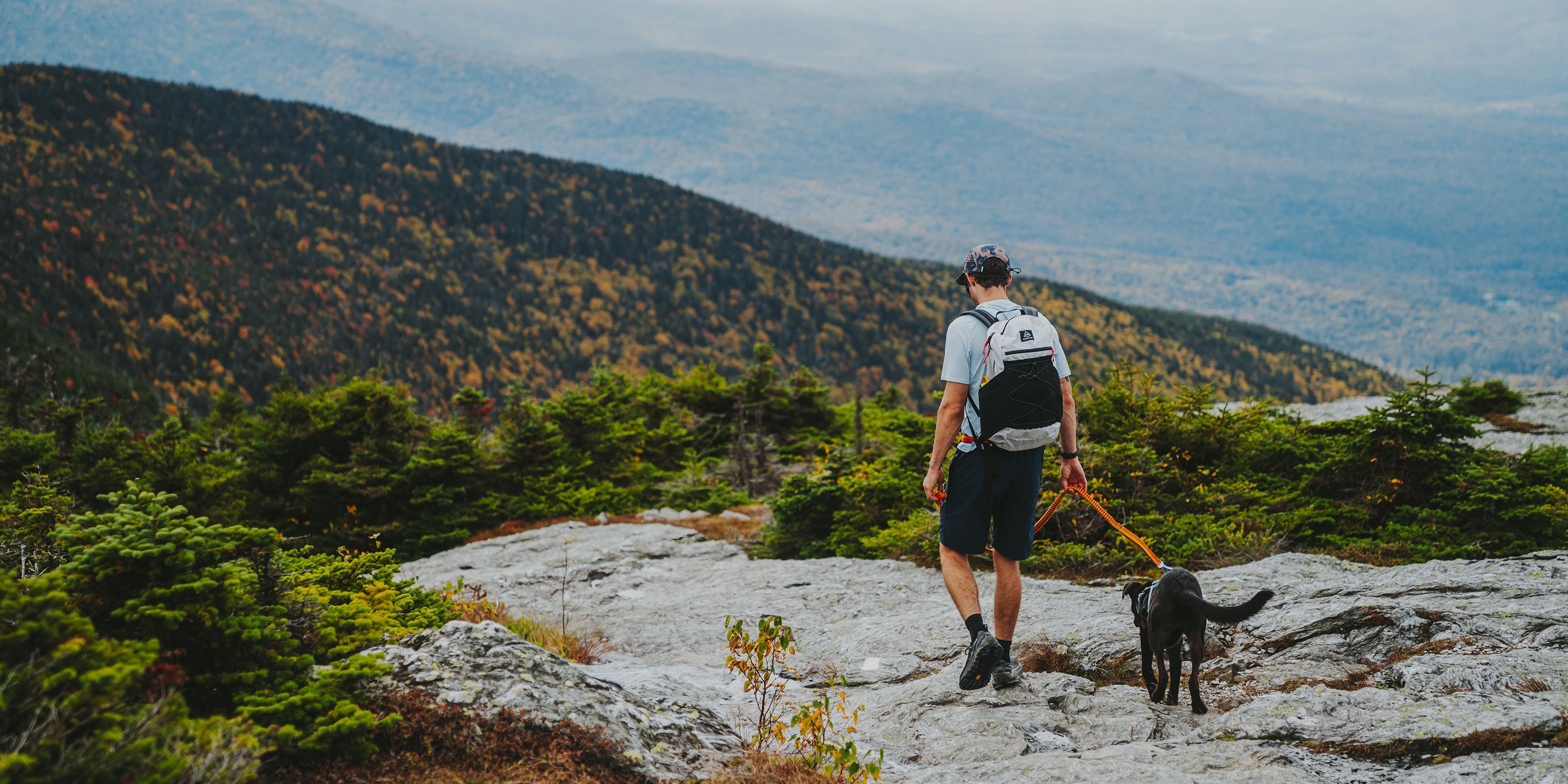 Man walking a dog on a leash with mountains in the background wearing a Hyperlite Mountain Gear Daybreak 22 pack