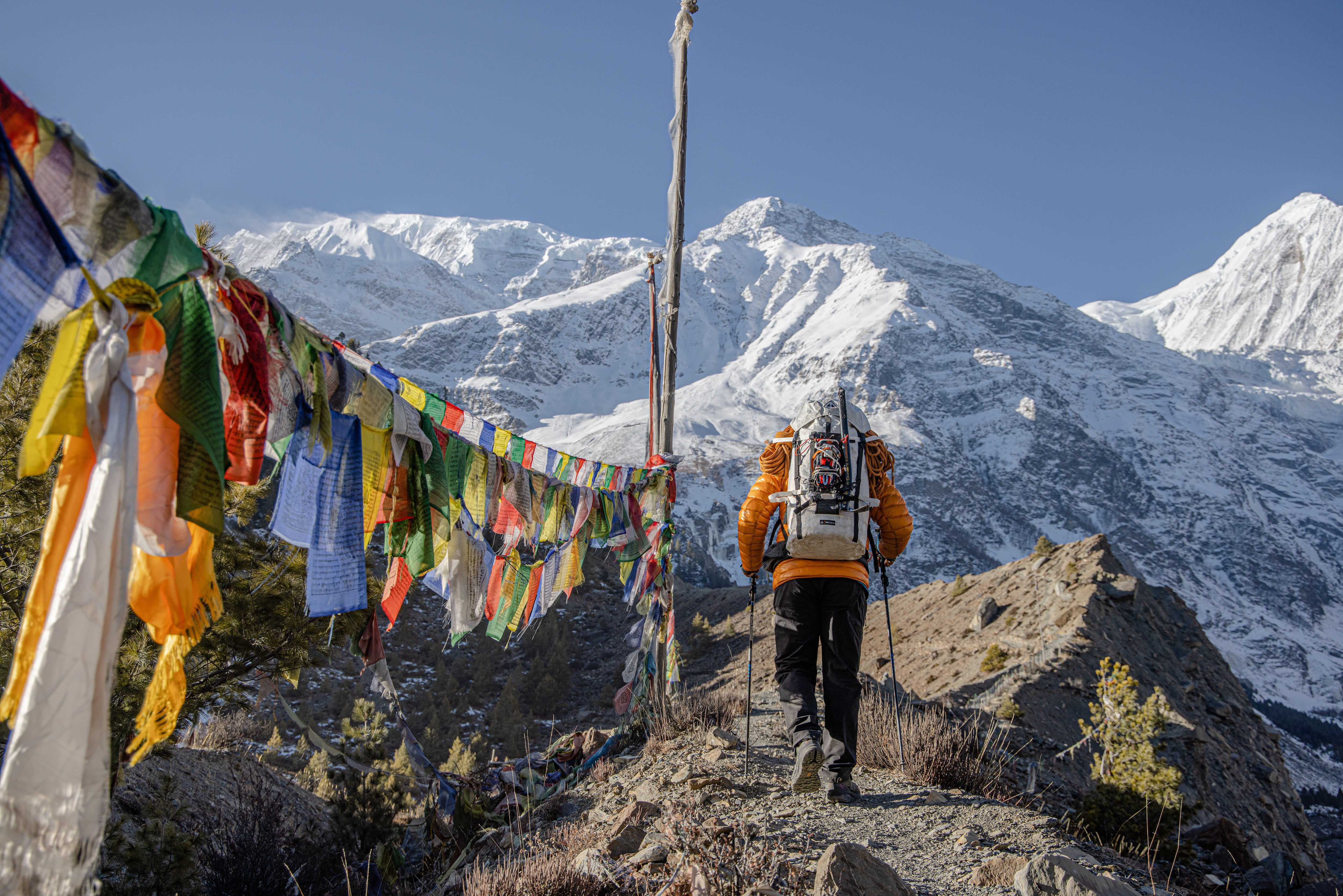 A man walking along a trail with prayer flags.