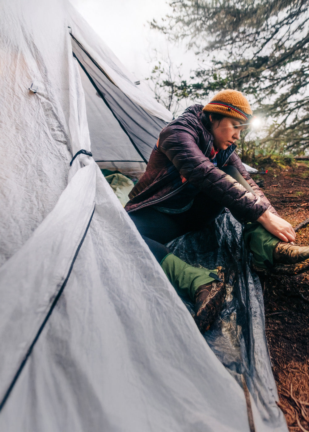 Person sitting outside a white tent in a forested area