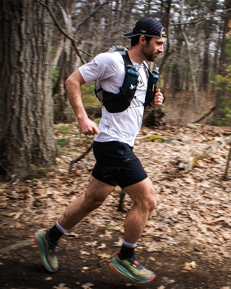 Will Peterson running on a trail in a forested area with the Pemi 15 running vest