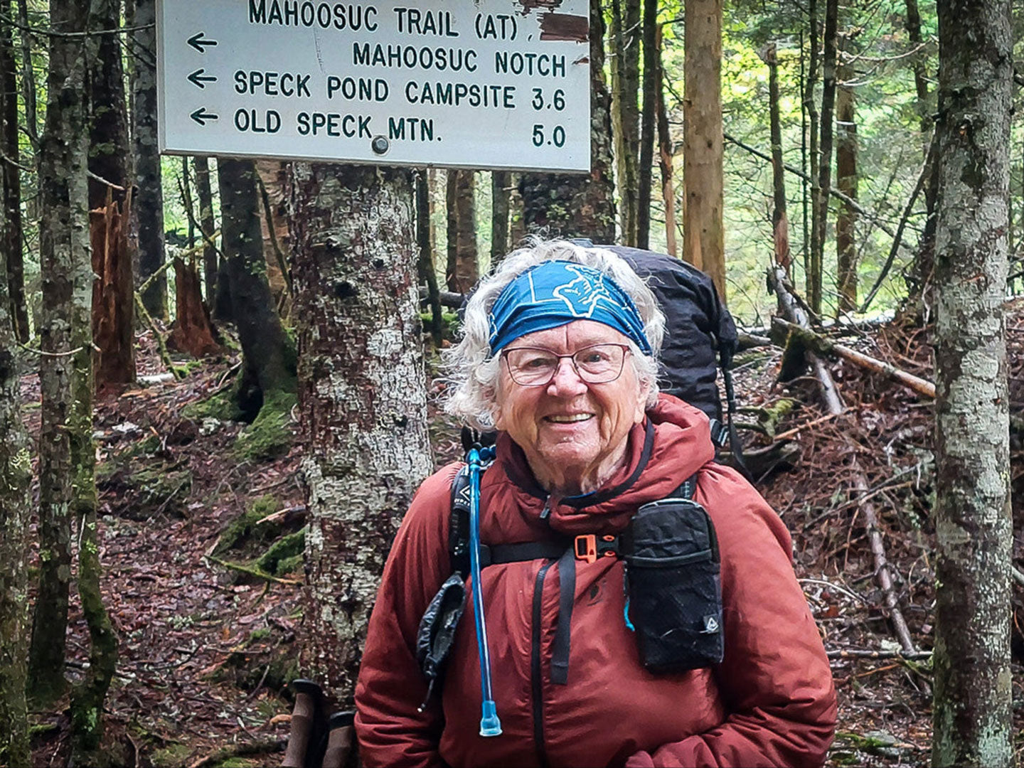 Person hiking in a forest with a trail sign in the background
