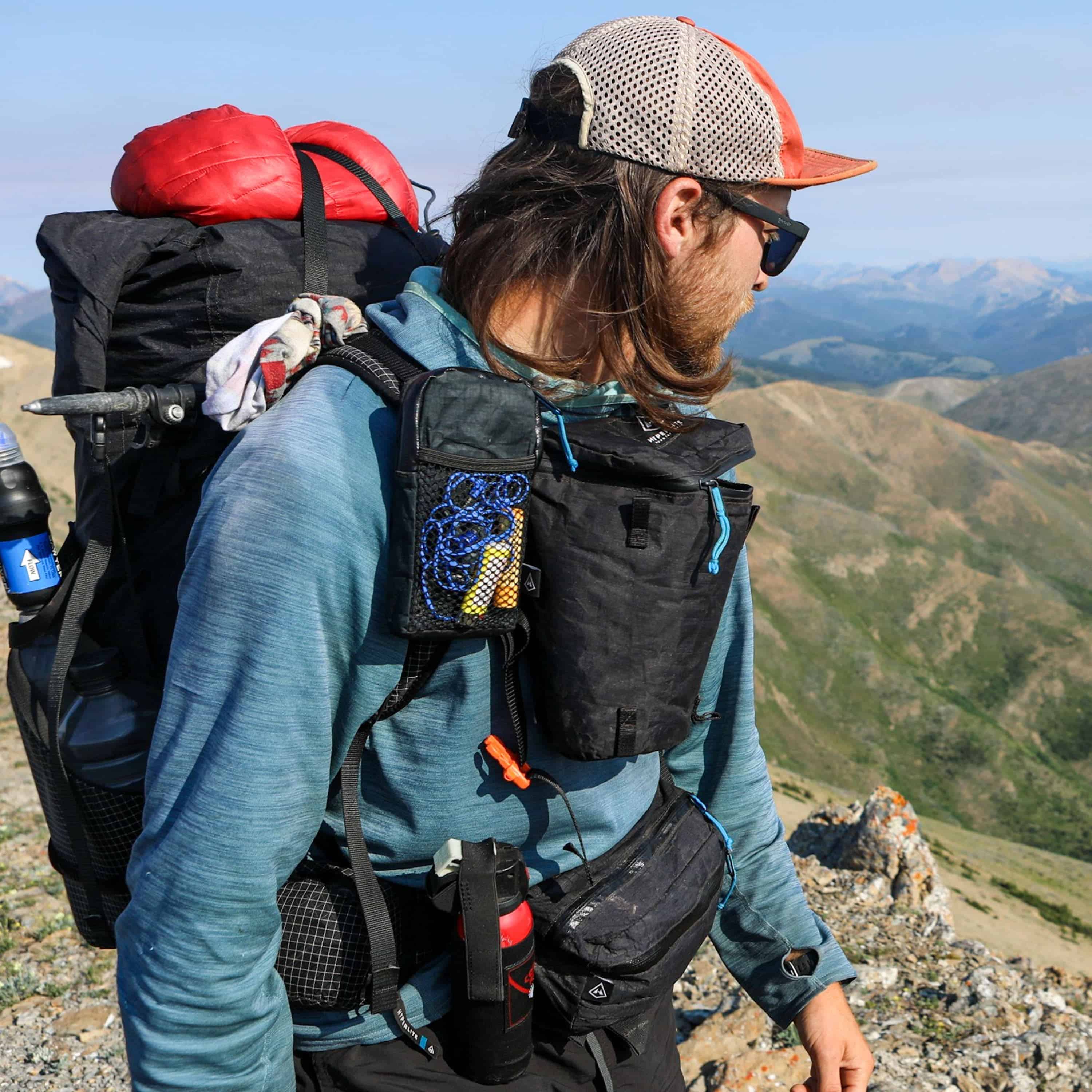 Hiker is shown with multiple accesories strapped to their pack including the Hyperlite Mountain Gear Camera Pod in Black