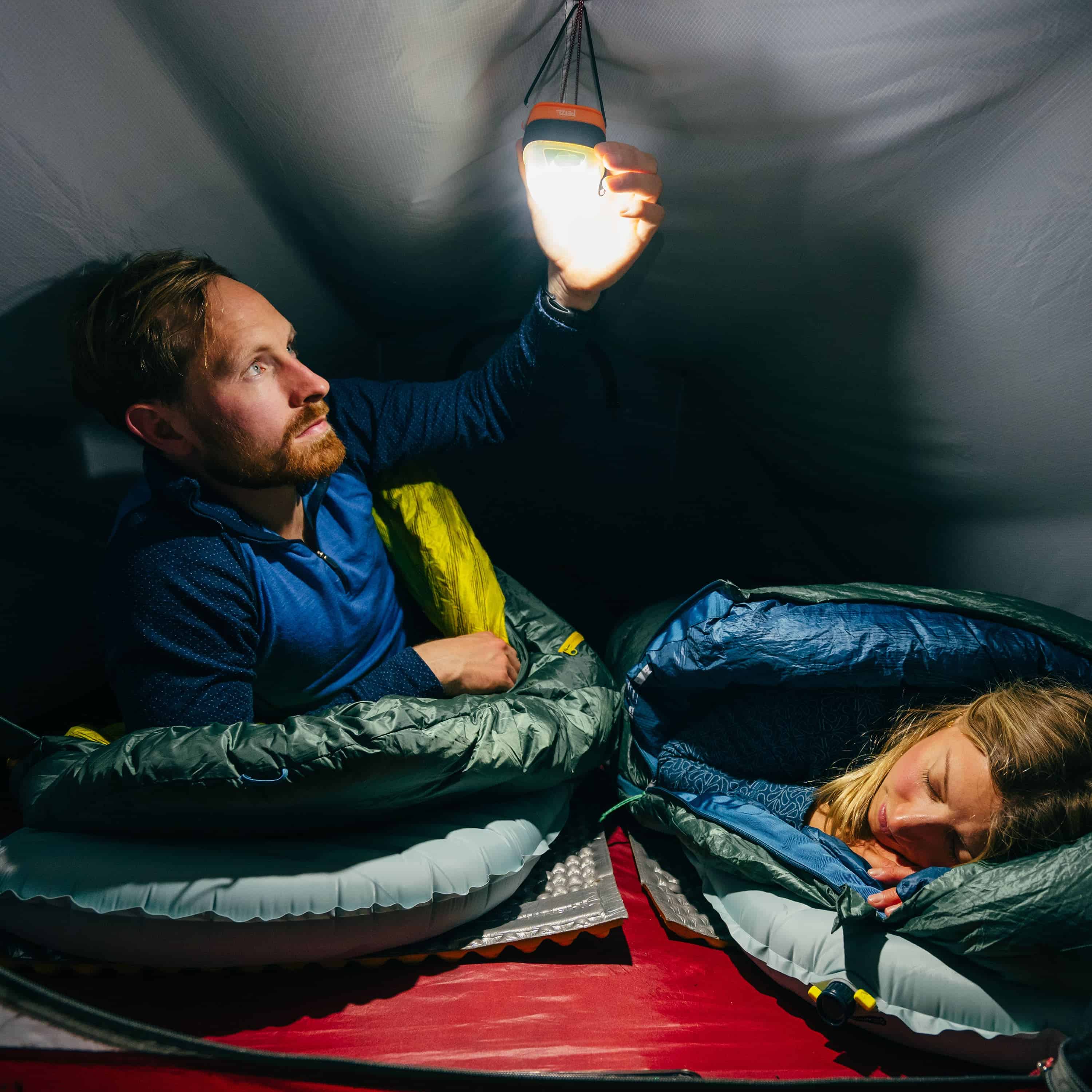 A camper lays on the Therm-a-Rest NeoAir® XTherm™ NXT Sleeping Pad in their tent while turning on an overhead lantern