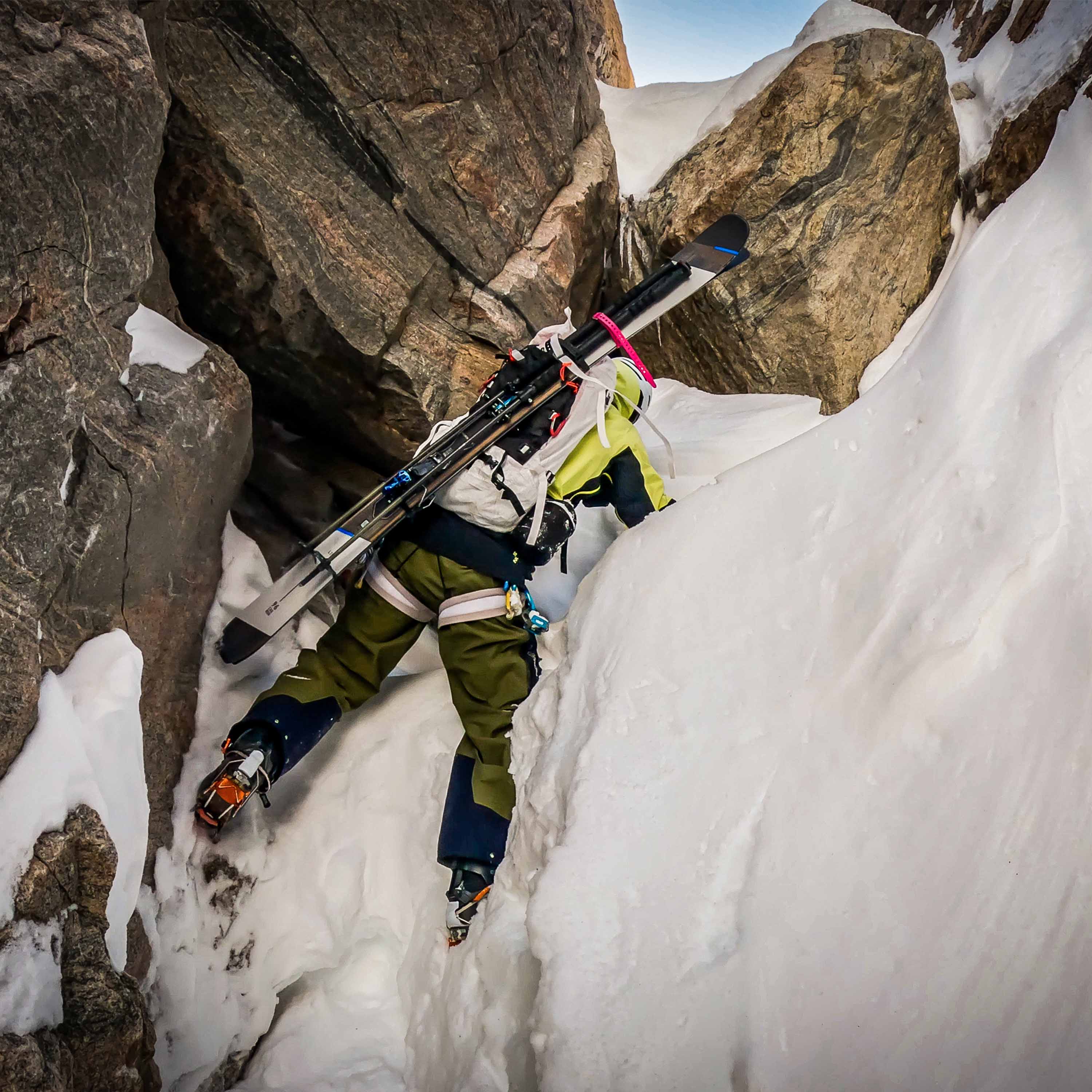 A mountaineer approaches the top of a snowy mountain with their skis attached using the Hyperlite Mountain Gear Diagonal Carry Kit