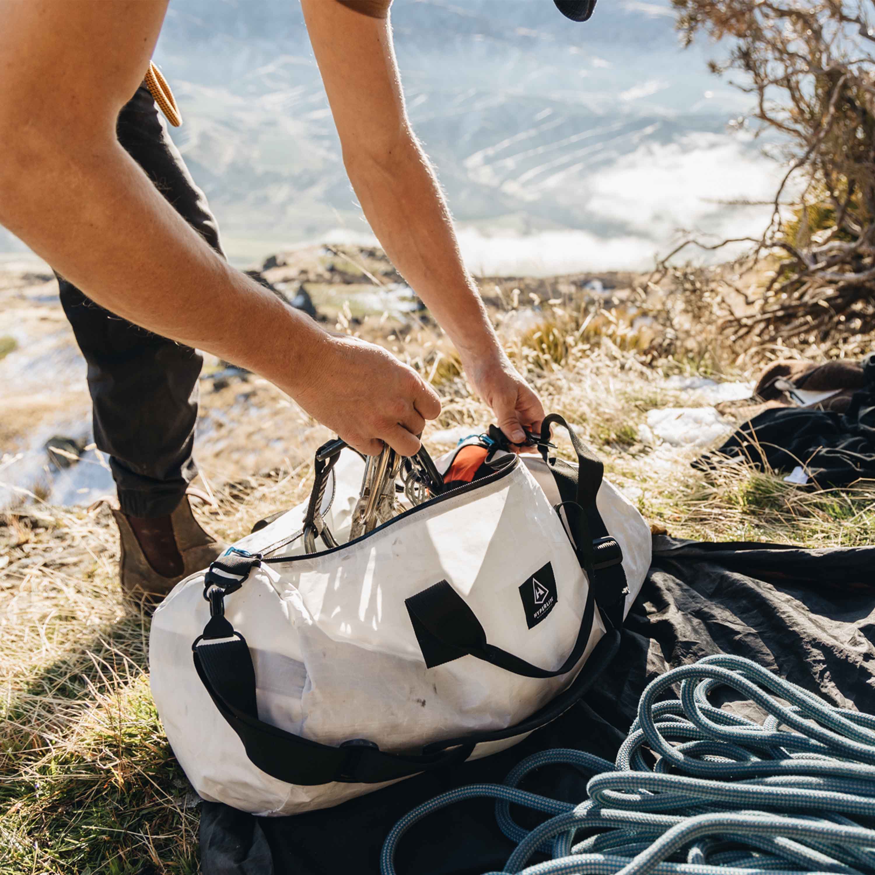 A climber taking gear out of the Hyperlite Mountain Gear 30L Approach Duffel in preparation to climb