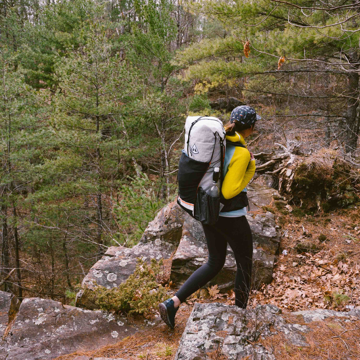 Hiker descends a rocky trail in the forest wearing the Hyperlite Mountain Gear Packs Unbound 55