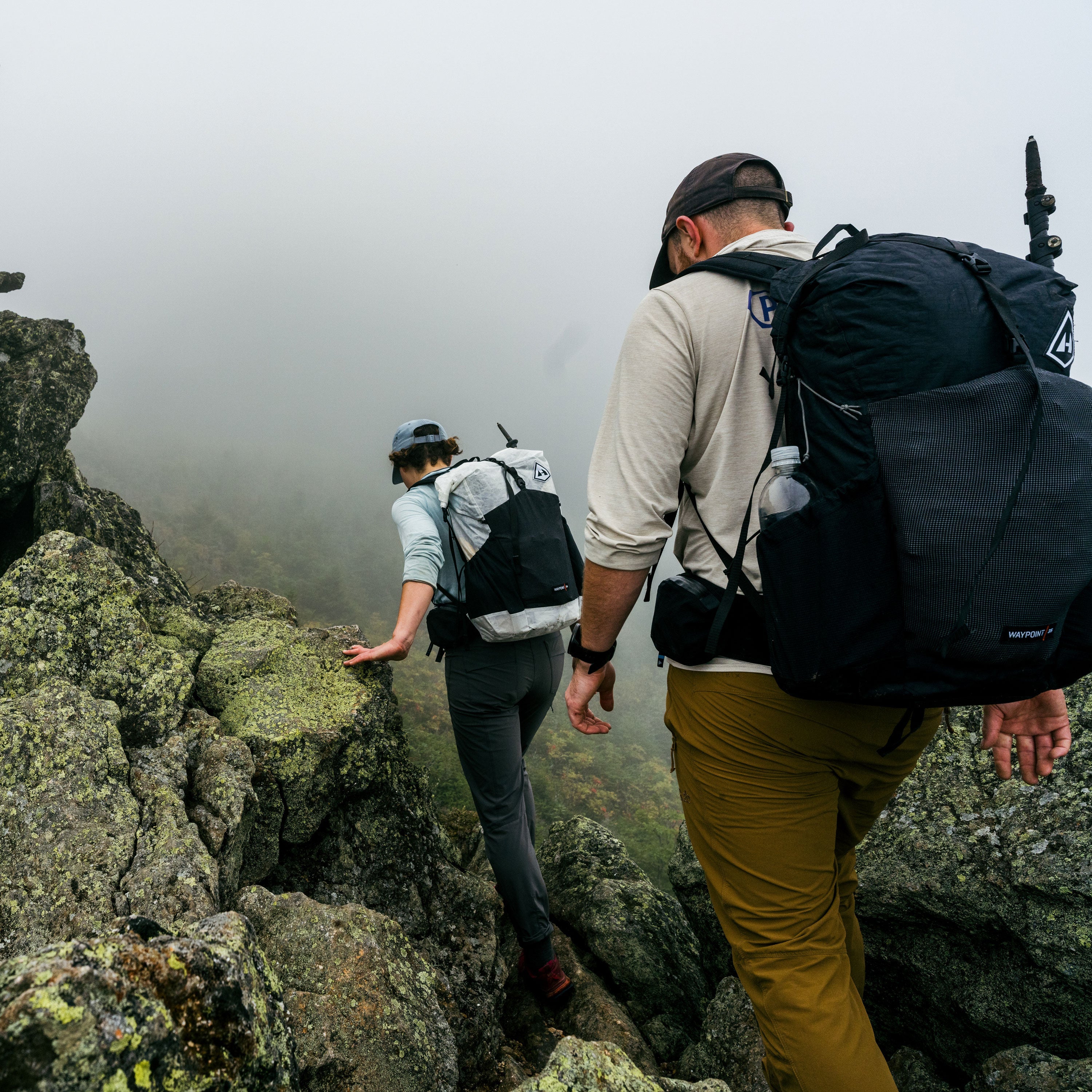 Hikers descend a rocky moss covered section of trail amidst thick fog wearing the Hyperlite Mountain Gear Waypoint 35