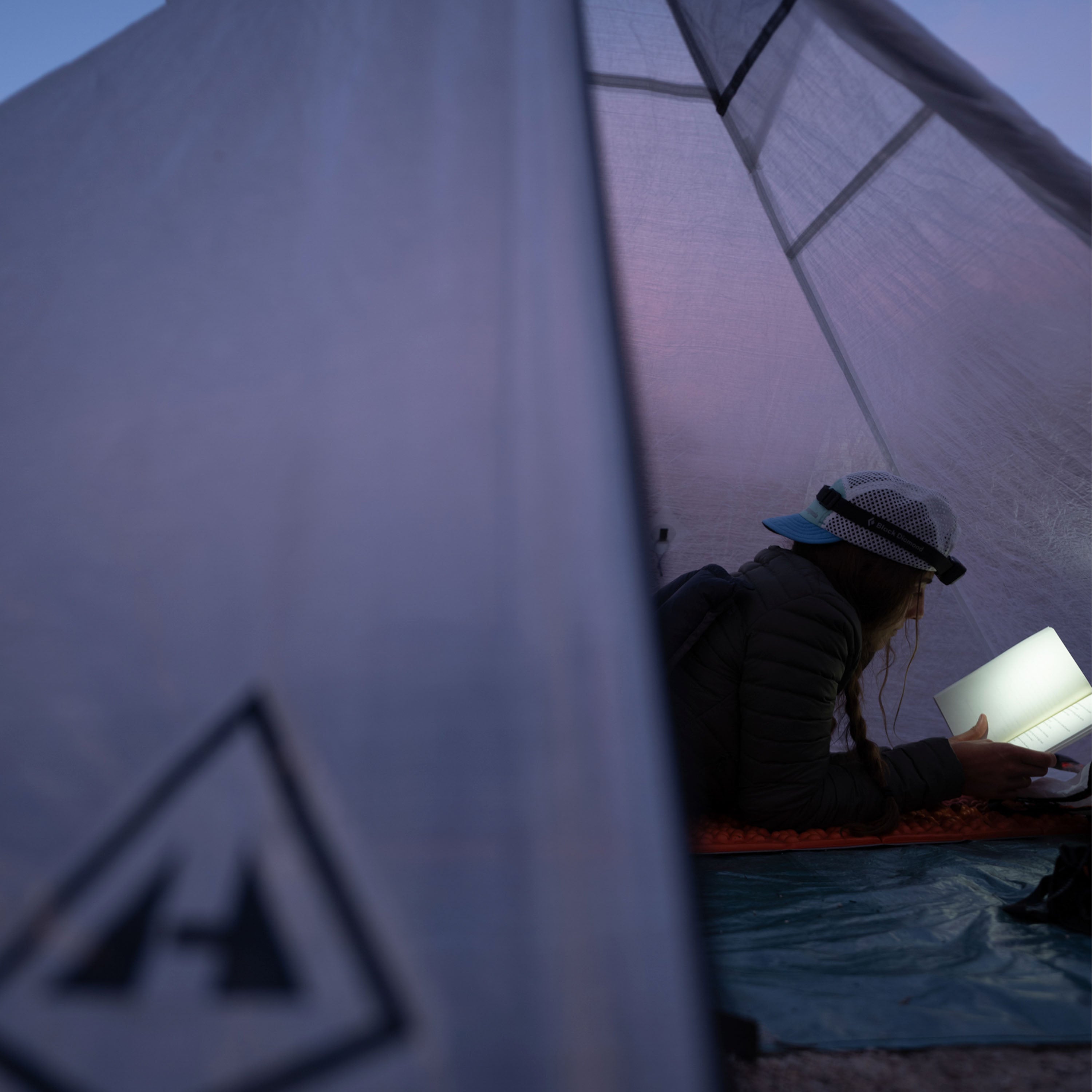 Close up view of the Hyperlite logo with a camper laying down inside the Hyperlite Mountain Gear Mid 1 Tarp