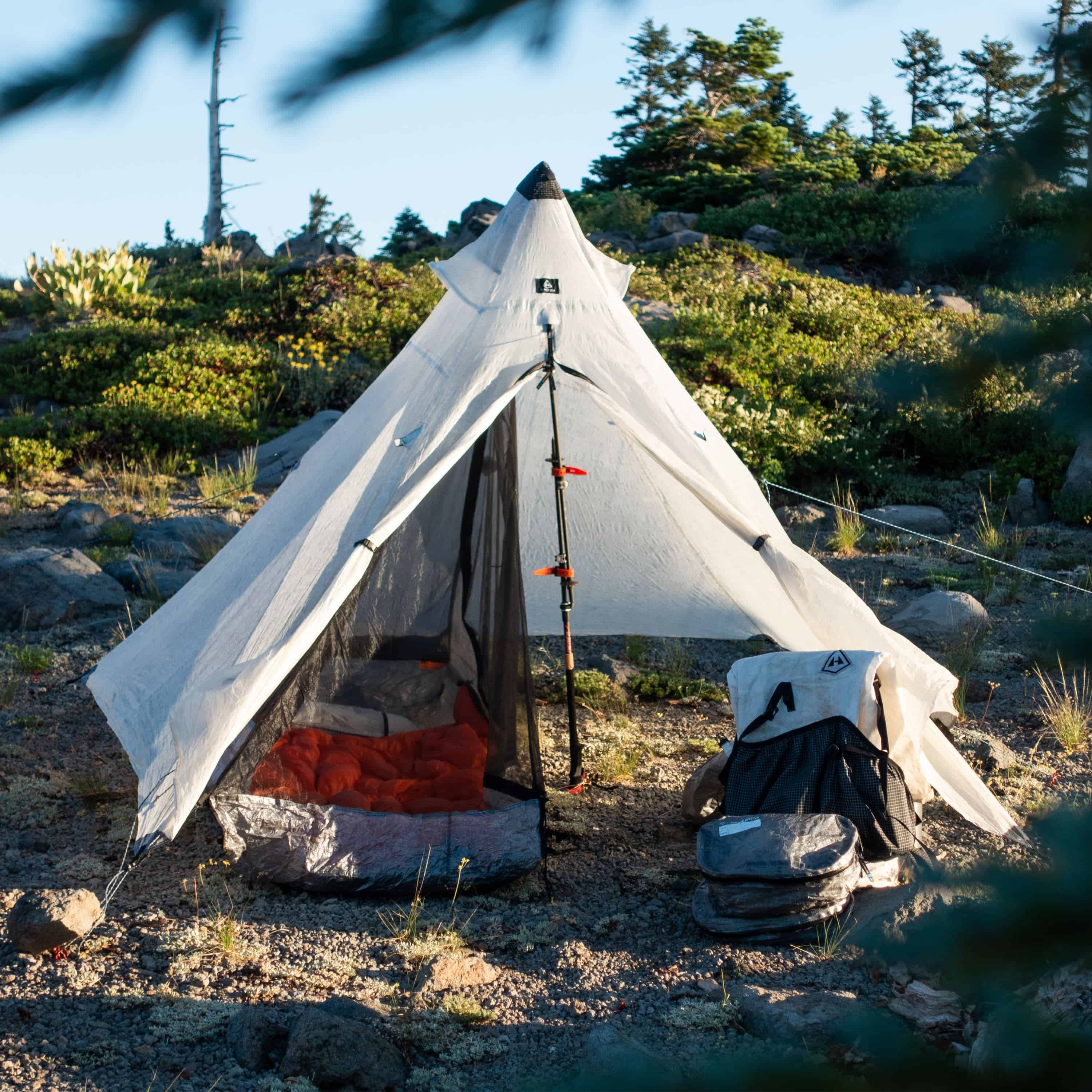 Exterior front view of Hyperlite Mountain Gear Shelters UltaMid 2 Half Insert in a clearing. A sleeping bag is inside, and a Hyperlite pack is sitting outside on the ground