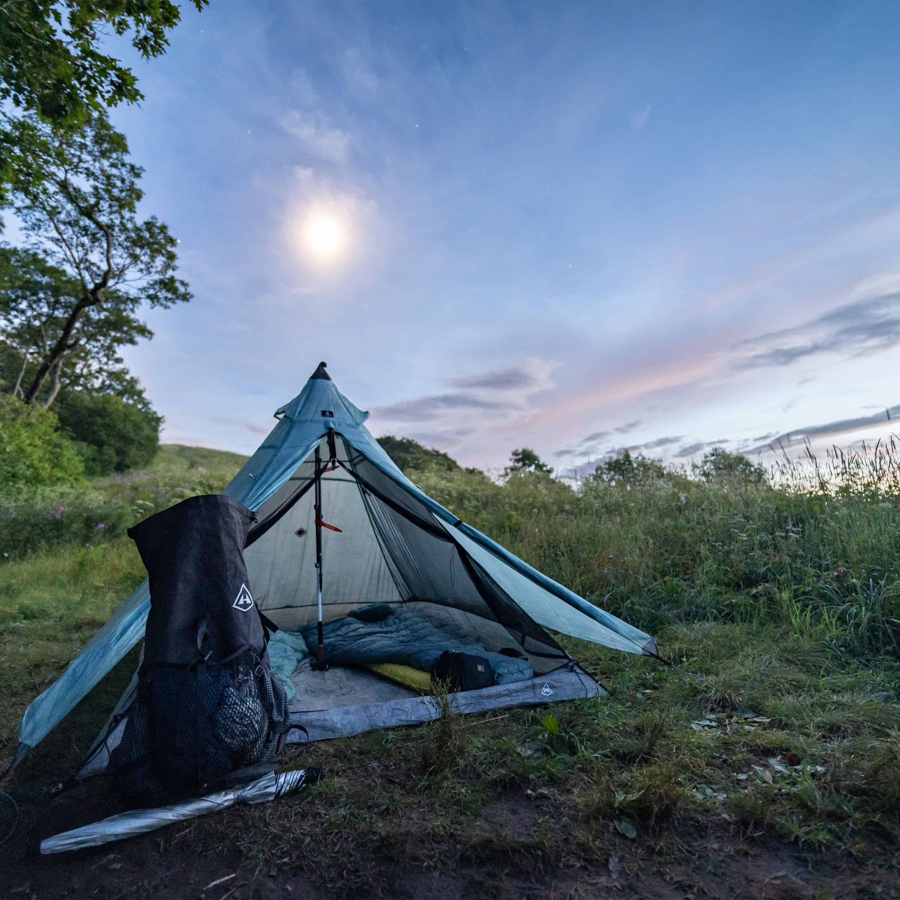 Exterior front view of Hyperlite Mountain Gear Shelters UltaMid 2 Insert with DCF11 Floor inside white tent in a grassy landscape at dusk