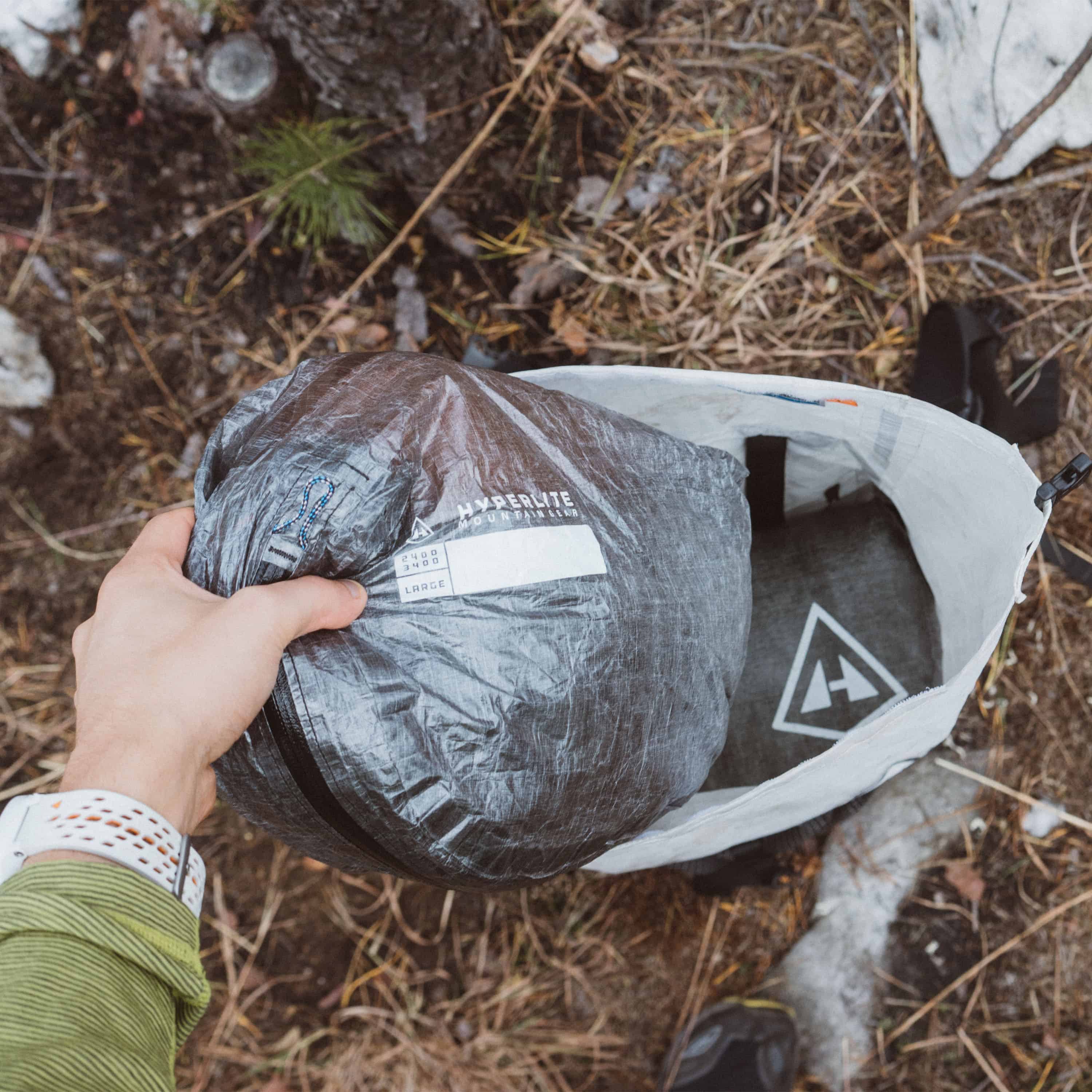 A person pulling a Hyperlite Mountain Gear Pod out of their ultralight pack