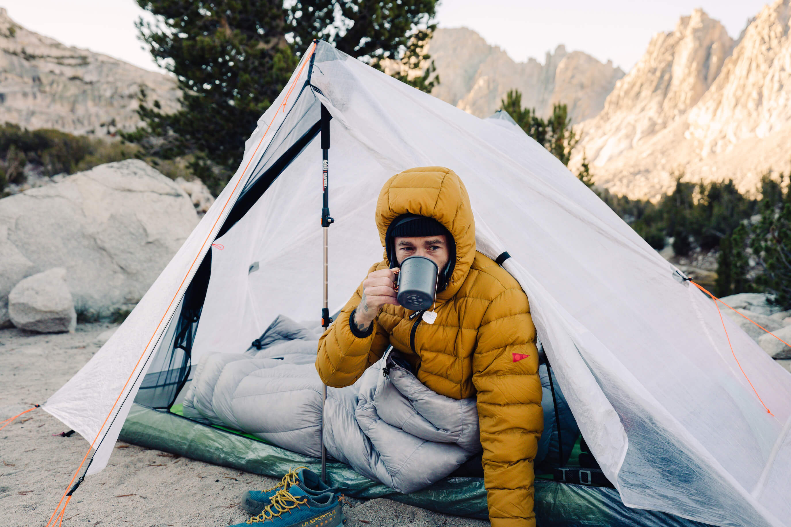 A man sitting in front of a tent with a cup of coffee.