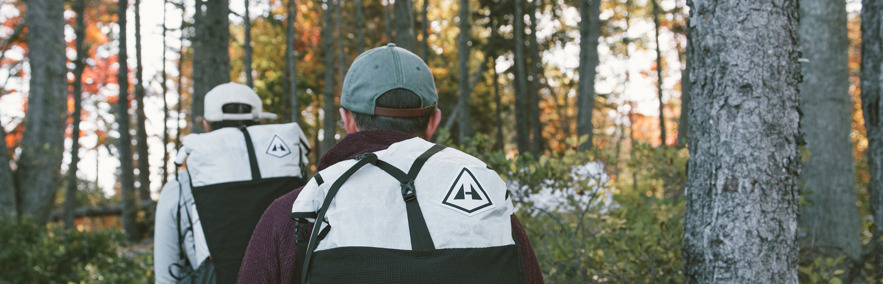 Two people walking through the woods with backpacks.