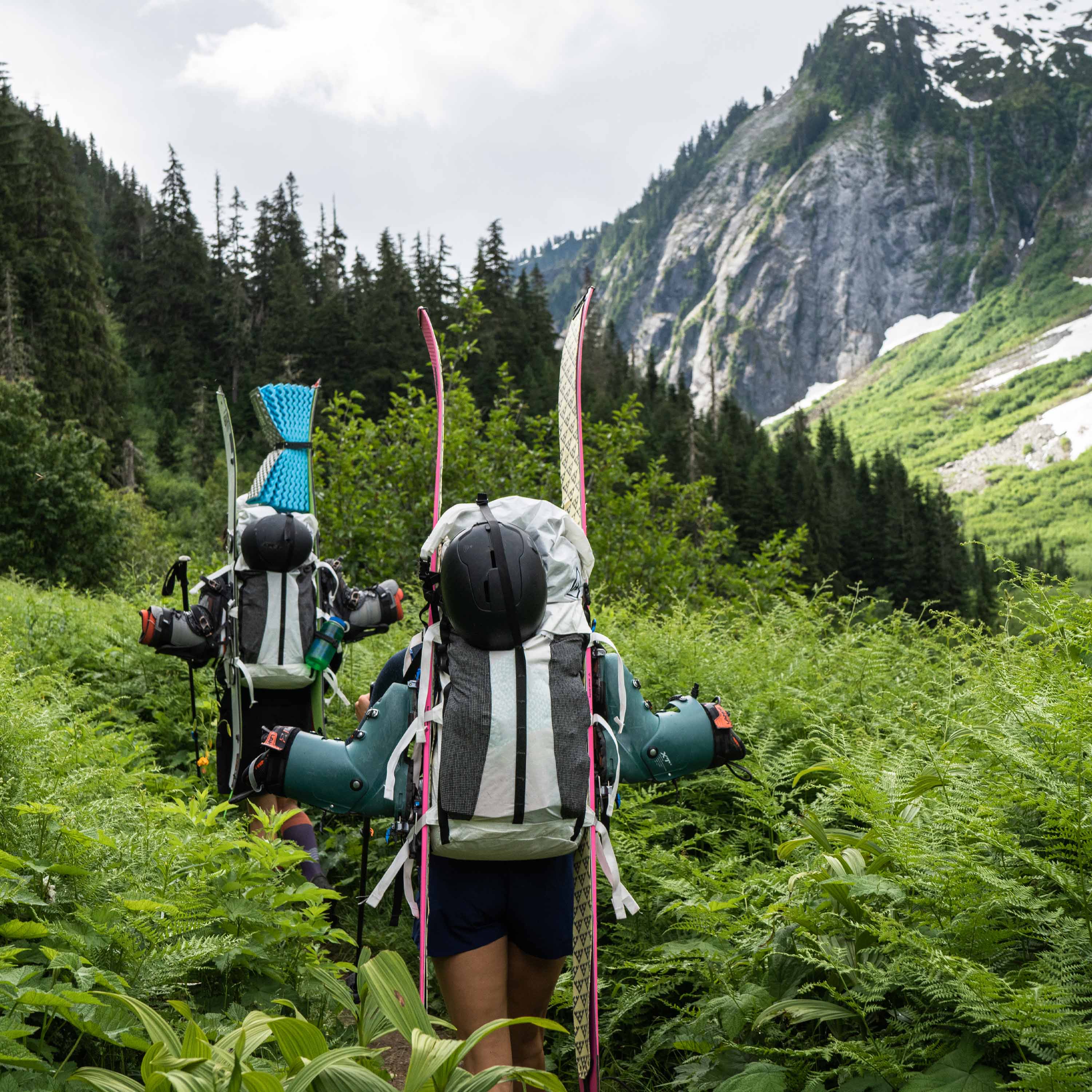 Hikers in the forest with skiis attached using the standard carry method on the Hyperlite Mountain Gear Headwall 55