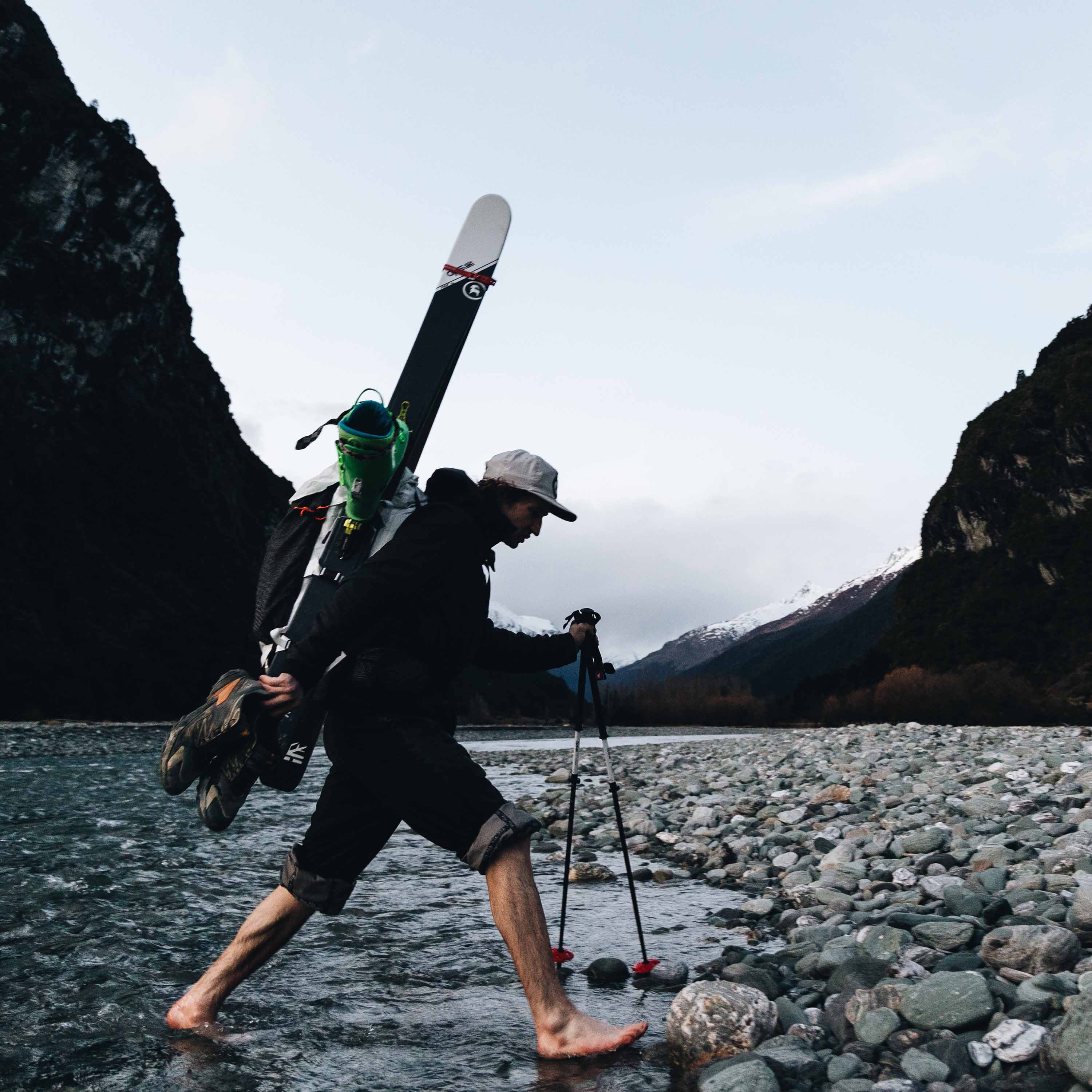 Barefoot hiker crosses a rocky stream with their Headwall 55 by Hyperlite Mountain Gear