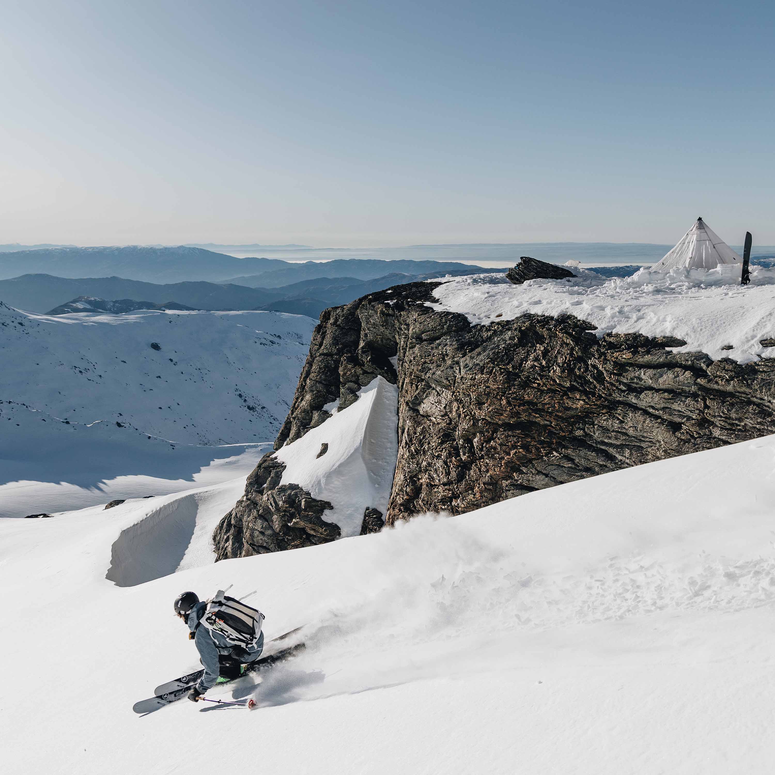 Skiier kicks up snow behind them as they descend the snowy mountain wearing the Hyperlite Mountain Gear Headwall 55