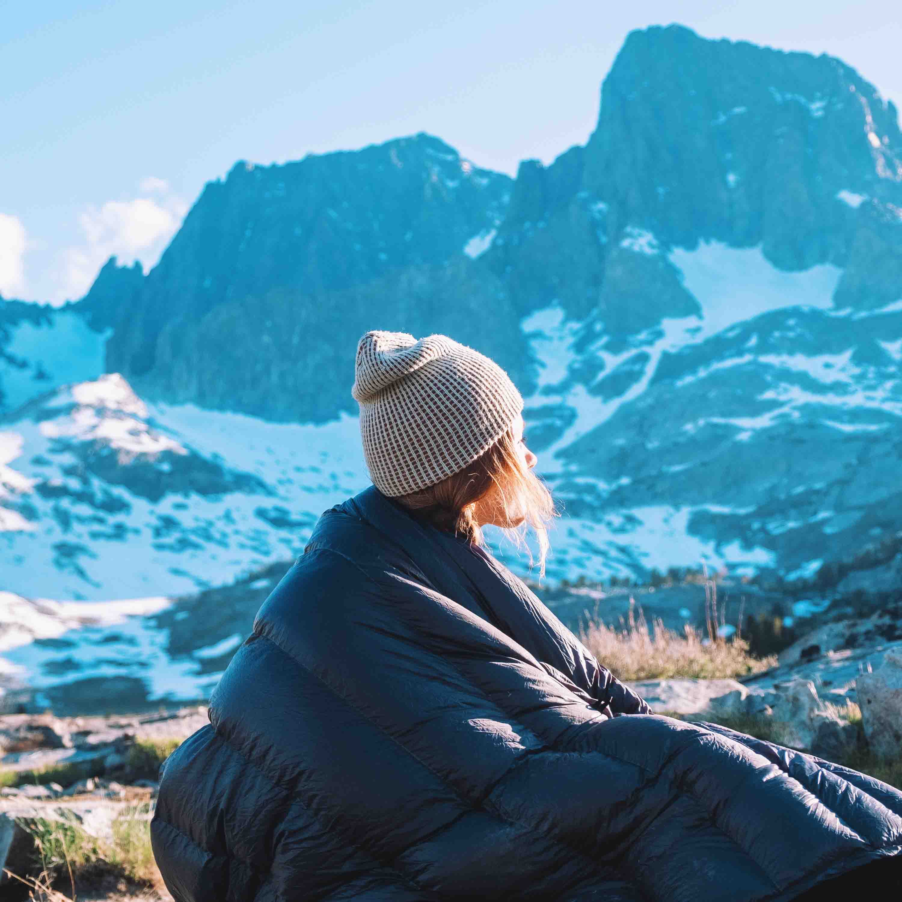 A hiker sits up inside of their Hyperlite Mountain Gear 40 Degree Quilt with snowy mountains in the background