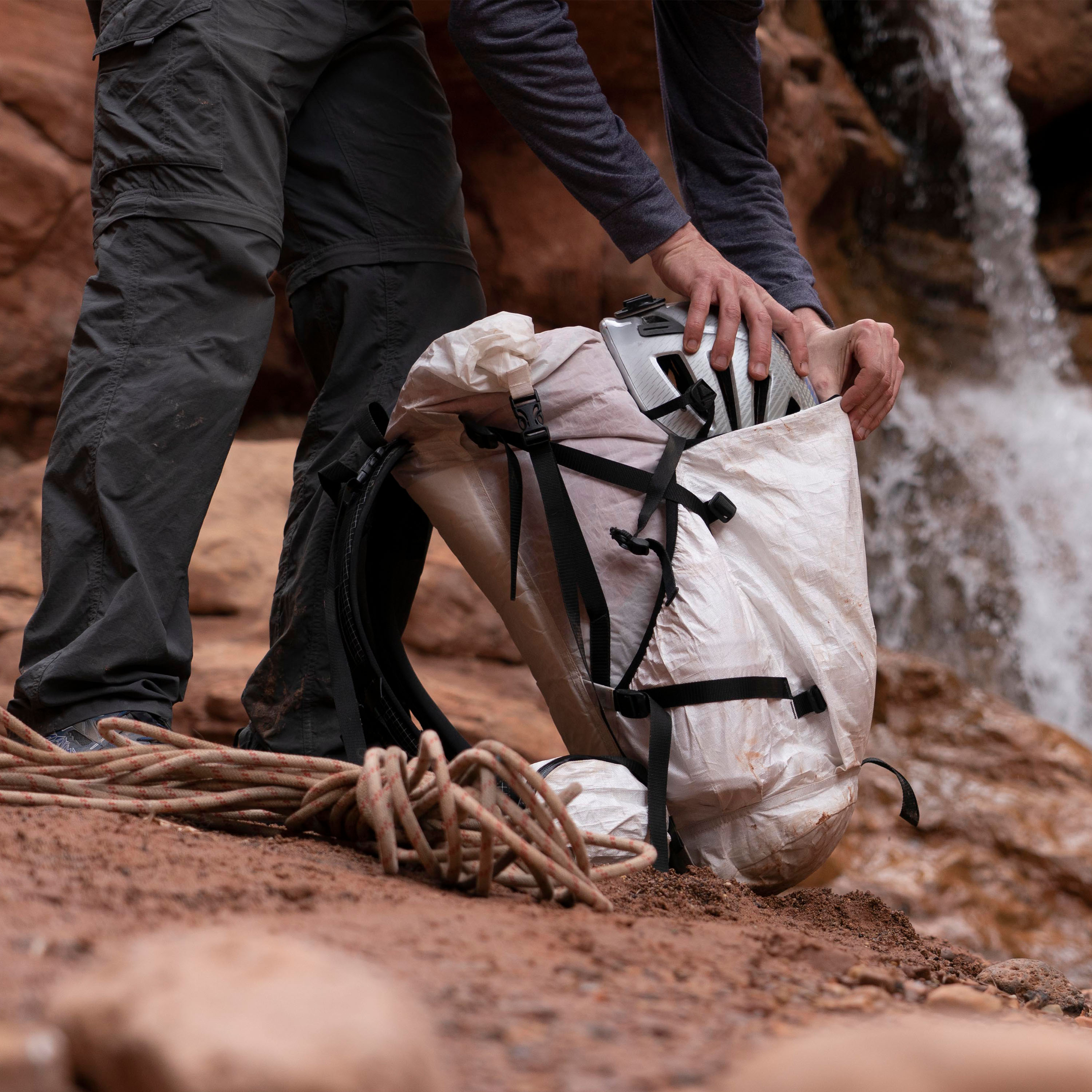 Hiker placing helmet into Hyperlite Mountain Gear's NorthRim 70 Pack in White