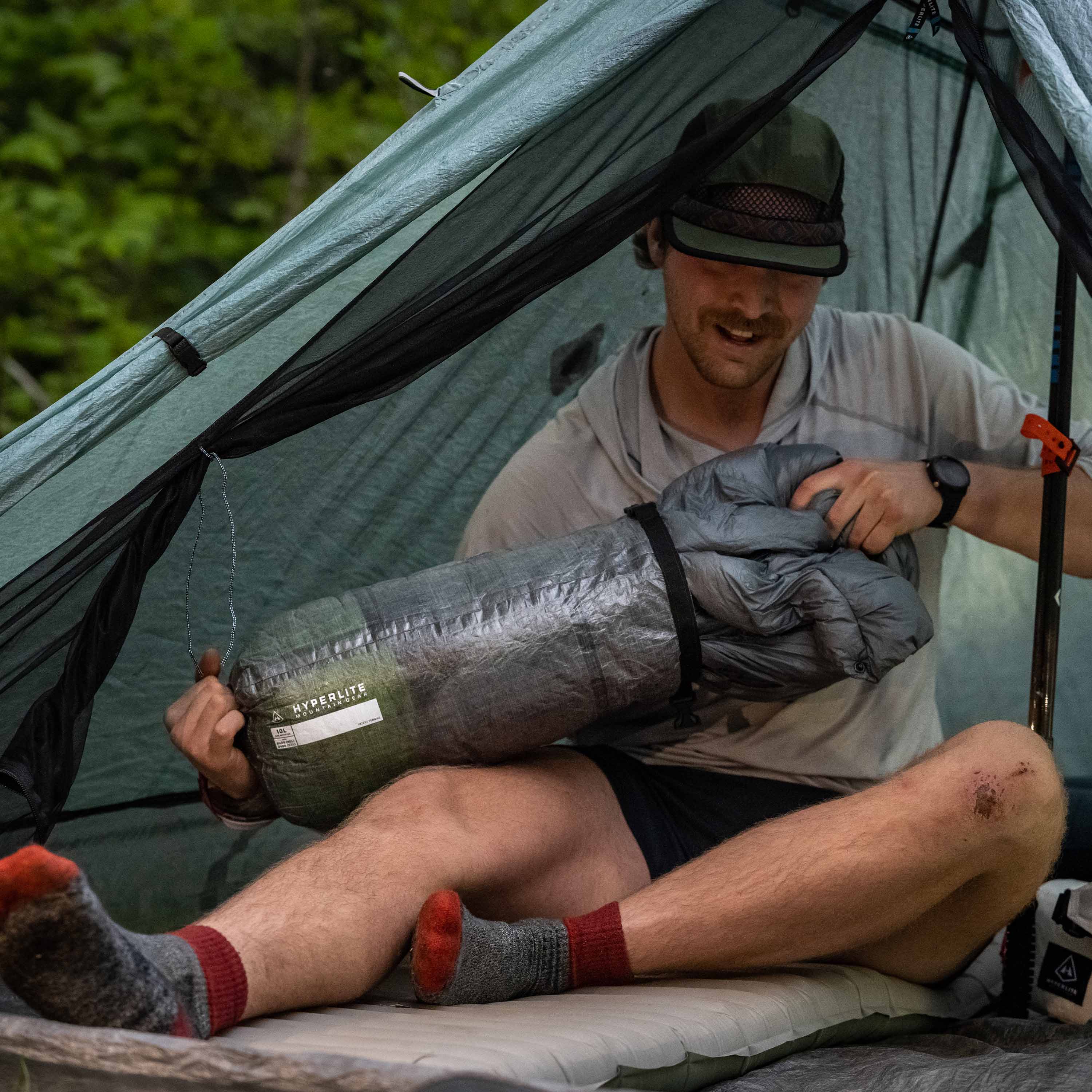 Camper pulling out their quilt from Hyperlite Mountain Gear's 10L Side Entry Pod in a tent