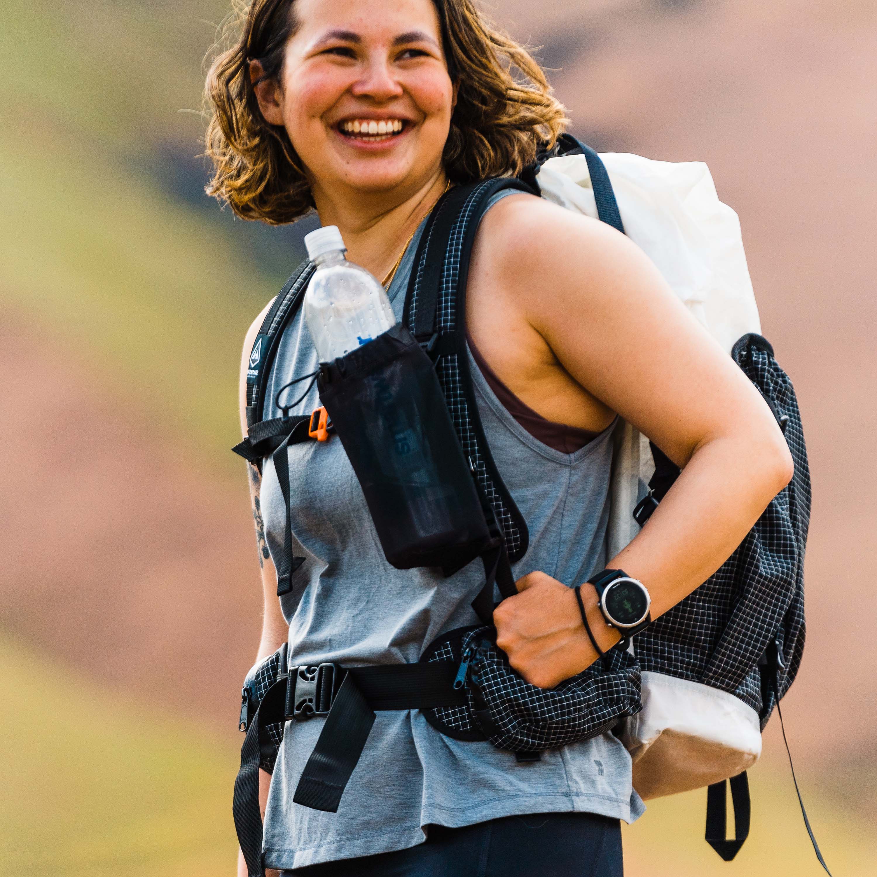 Hiker wearing Hyperlite Mountain Gear The Bottle Pocket attached to shoulder straps of backpack