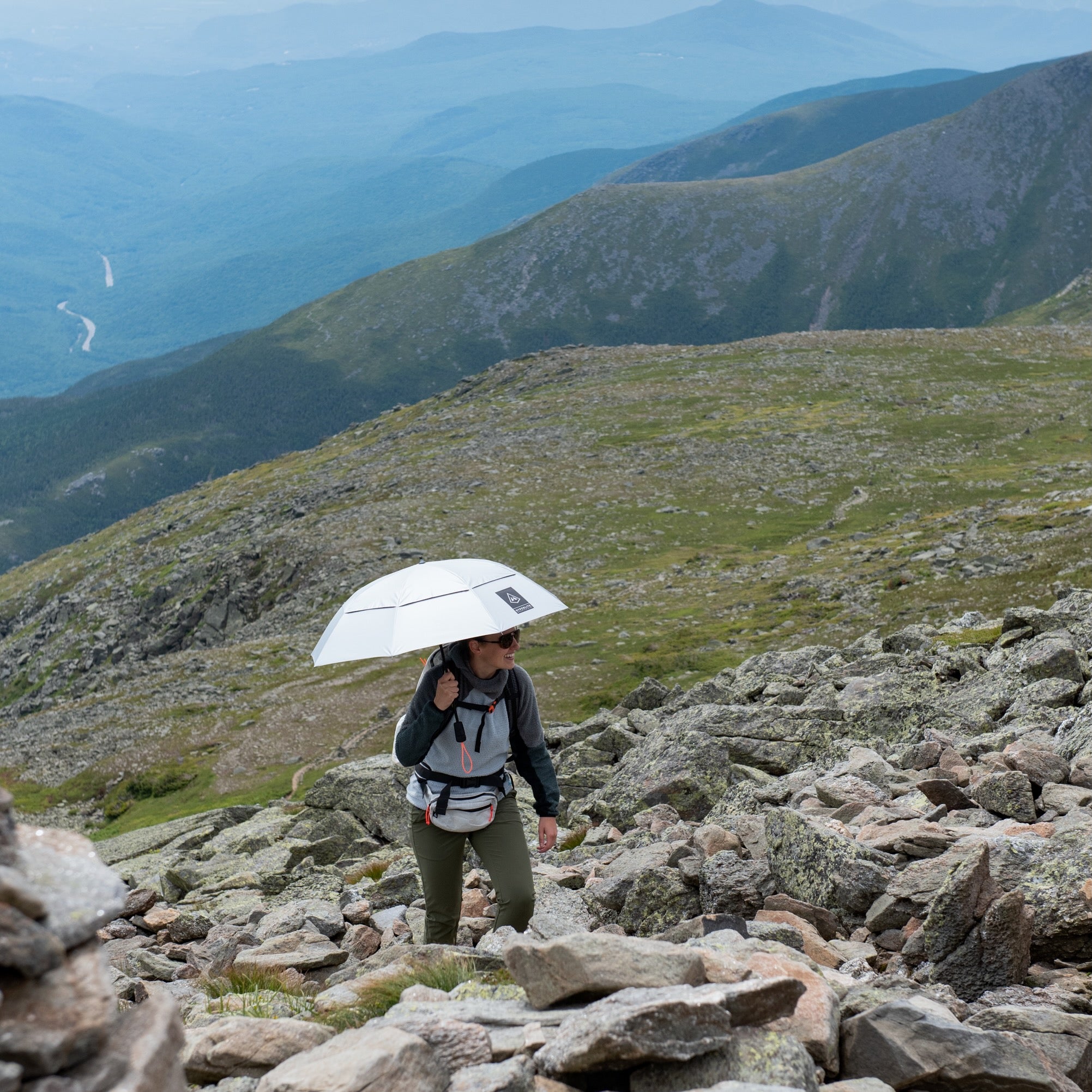 A hiker using the Hyperlite Mountain Gear Runabout Bundle walks up a rocky trail towards the peak